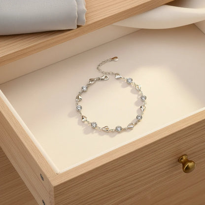 Drawer flat-lay of the Silver Heart Crystal Tennis Bracelet arranged neatly inside a wooden jewelry drawer, with folded fabric nearby, highlighting the elegant design and luxe sparkle of the silver hearts and crystal stones | Oria Jewel