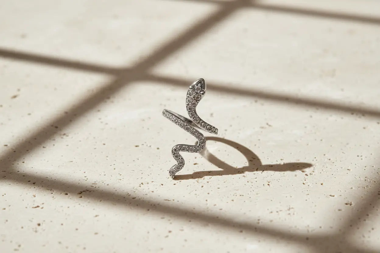 Silver Pavé Snake Wrap Ring standing upright on a speckled stone surface under window-grid shadows, showcasing the curved wrap shape, snake head detail, and pavé crystals | OriaJewel