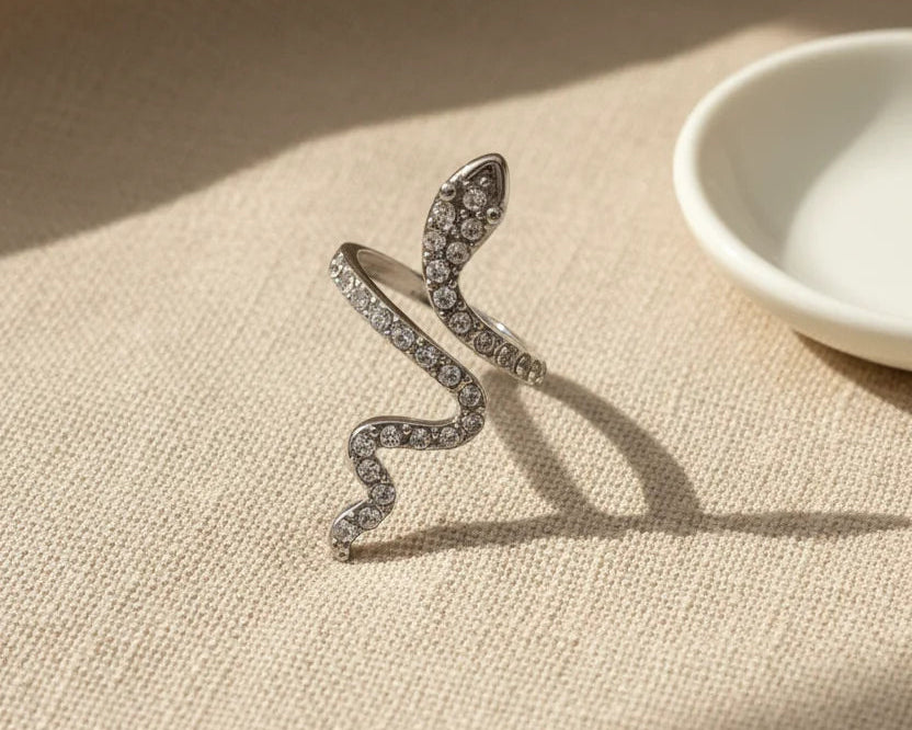 Silver Pavé Snake Wrap Ring close-up on textured beige fabric near a white dish, warm sunlight catching the pavé stones along the snake body and head | OriaJewel