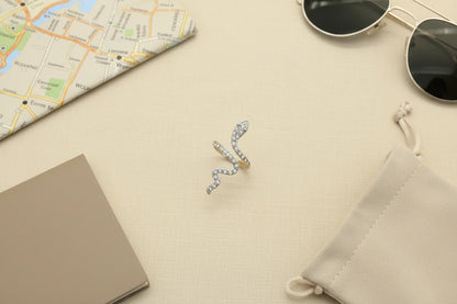 Silver Pavé Snake Wrap Ring flat-lay on a neutral linen surface with a map, sunglasses, notebook, and drawstring pouch, travel-inspired styling with the ring centered as the hero | OriaJewel
