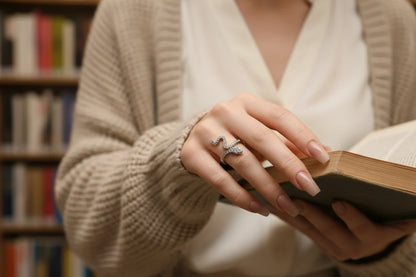 Silver Pavé Snake Wrap Ring worn while holding an open book in a cozy library setting, focus on the sparkling snake wrap ring and manicured hand with soft bokeh background | OriaJewel