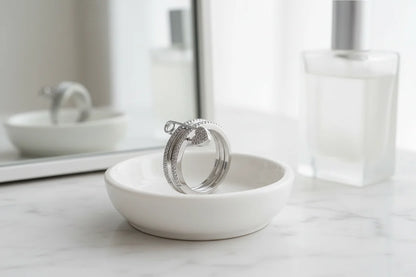 Silver Safety Pin Ring displayed in a white ceramic dish on a marble vanity with soft bathroom lighting, blurred mirror and perfume bottle in the background | OriaJewel