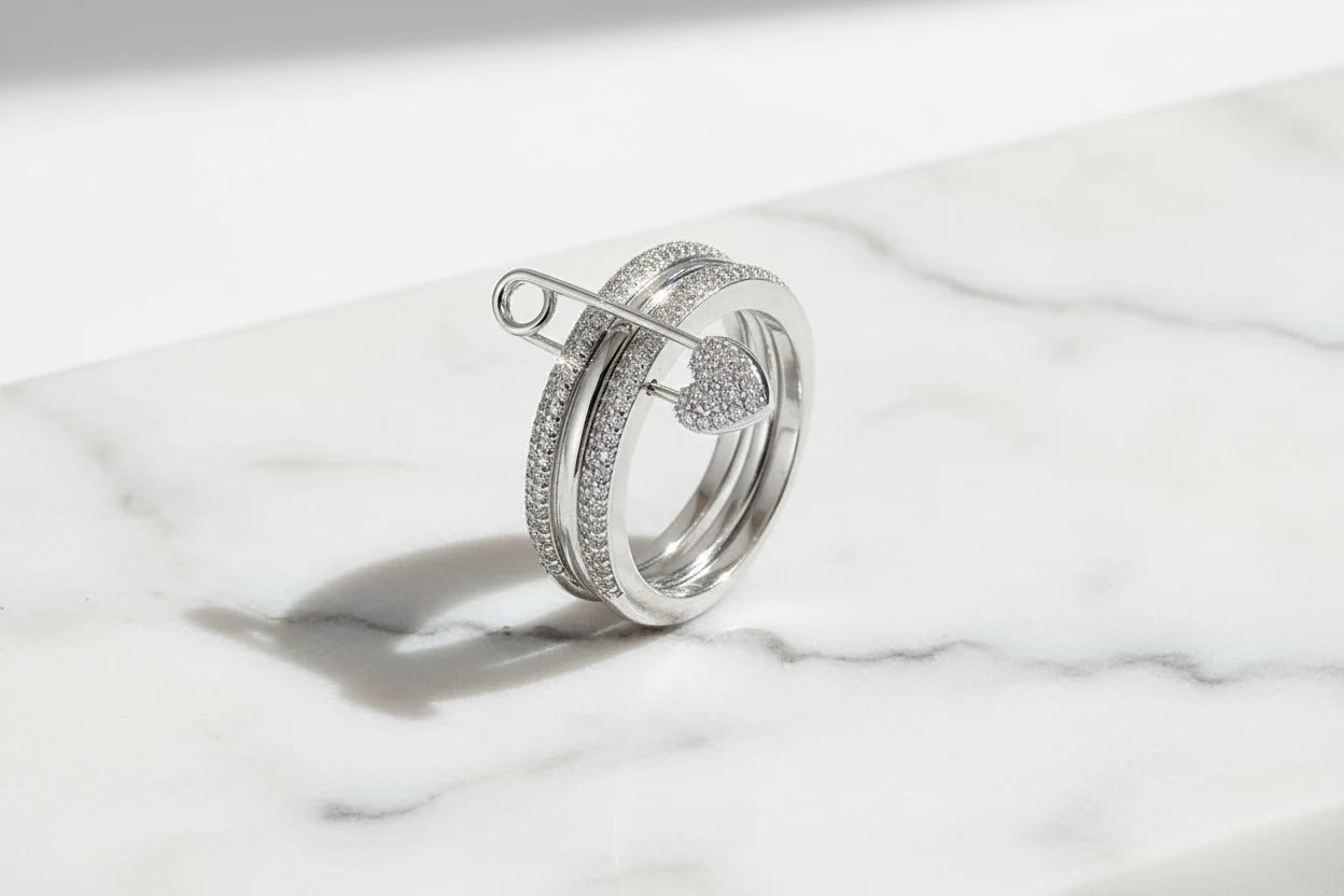Silver Safety Pin Ring on a white marble slab in bright natural light, pavé bands and heart-shaped pin clasp in sharp focus with a clean shadow | OriaJewel