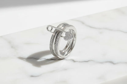 Silver Safety Pin Ring on a white marble slab in bright natural light, pavé bands and heart-shaped pin clasp in sharp focus with a clean shadow | OriaJewel