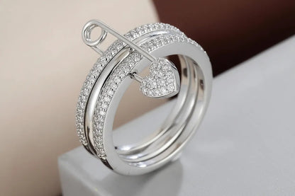 Macro close-up of Silver Safety Pin Ring on a light stone block, sparkling pavé triple bands and crystal heart charm across the front, high-detail finish | OriaJewel