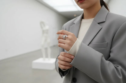Silver Safety Pin Ring styled on hand with a grey blazer in a modern gallery setting, minimal white background with soft sculpture blur, elegant fashion lifestyle vibe | OriaJewel