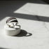 Studio product shot of a Silver bypass ring on a white round stand over marble, with dramatic sunlight and crisp shadows highlighting the pavé curve | OriaJewel
