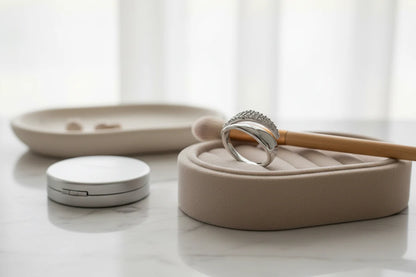 Silver bypass ring displayed on a beige jewelry tray beside a makeup brush and compact on a clean marble vanity, bright window light emphasizing the polished bypass design | OriaJewel
