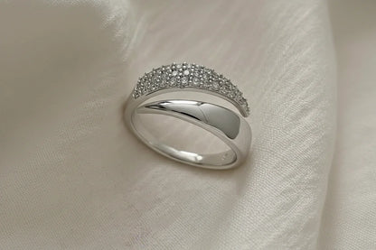 Macro close-up of a Silver bypass ring resting on ivory satin fabric, showing the pavé-studded arc and smooth overlapping bypass band in soft light | OriaJewel