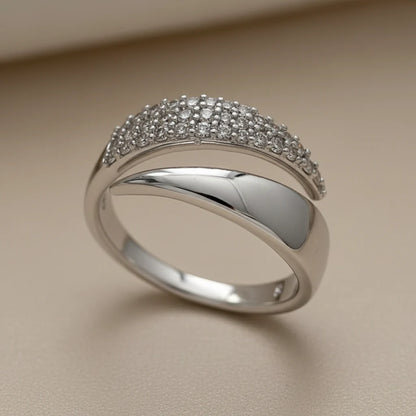 Close-up front angle of a Silver bypass ring on a warm beige background, focusing on the sparkling pavé top and mirror-finish crossover band | OriaJewel