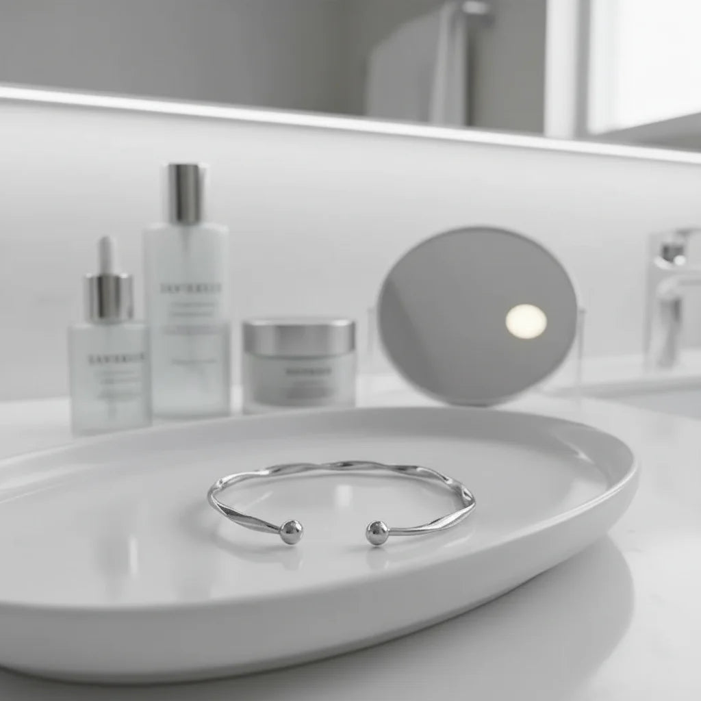 Silver twisted cuff bracelet styled on a glossy white bathroom tray, surrounded by minimal skincare bottles and a mirror for a clean, spa-like look | Oria Jewel