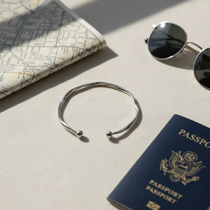 Travel-inspired flatlay featuring a Silver twisted cuff bracelet beside a folded city map, round sunglasses, and a navy passport on a cream surface | Oria Jewel