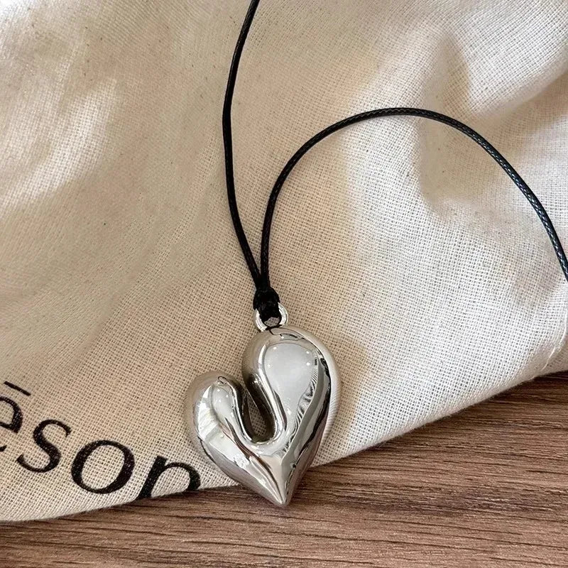 Simple Heart Pendant Necklace on a black cord resting on a beige fabric background | Oria Jewel