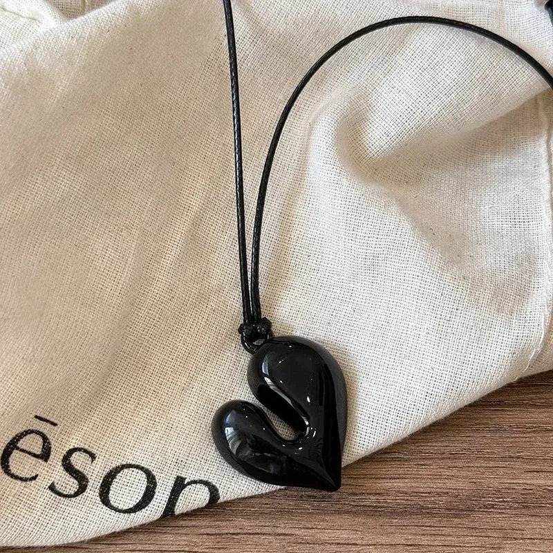 Simple Heart Pendant Necklace on a black cord, placed on a neutral fabric background | Oria Jewel