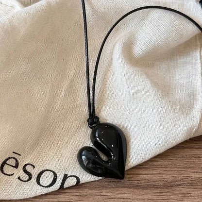 Simple Heart Pendant Necklace on a black cord, placed on a neutral fabric background | Oria Jewel
