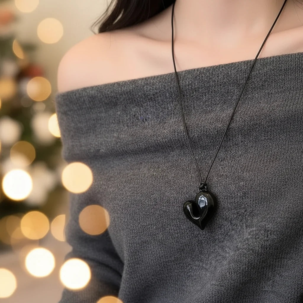 Simple Heart Pendant Necklace worn by a woman with a cozy off-shoulder sweater, with bokeh lights in the background | Oria Jewel