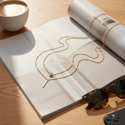 Cozy lifestyle flat lay of gold Star Layered Necklace resting on an open magazine beside sunglasses, coffee cup, and remote | Oria Jewel
