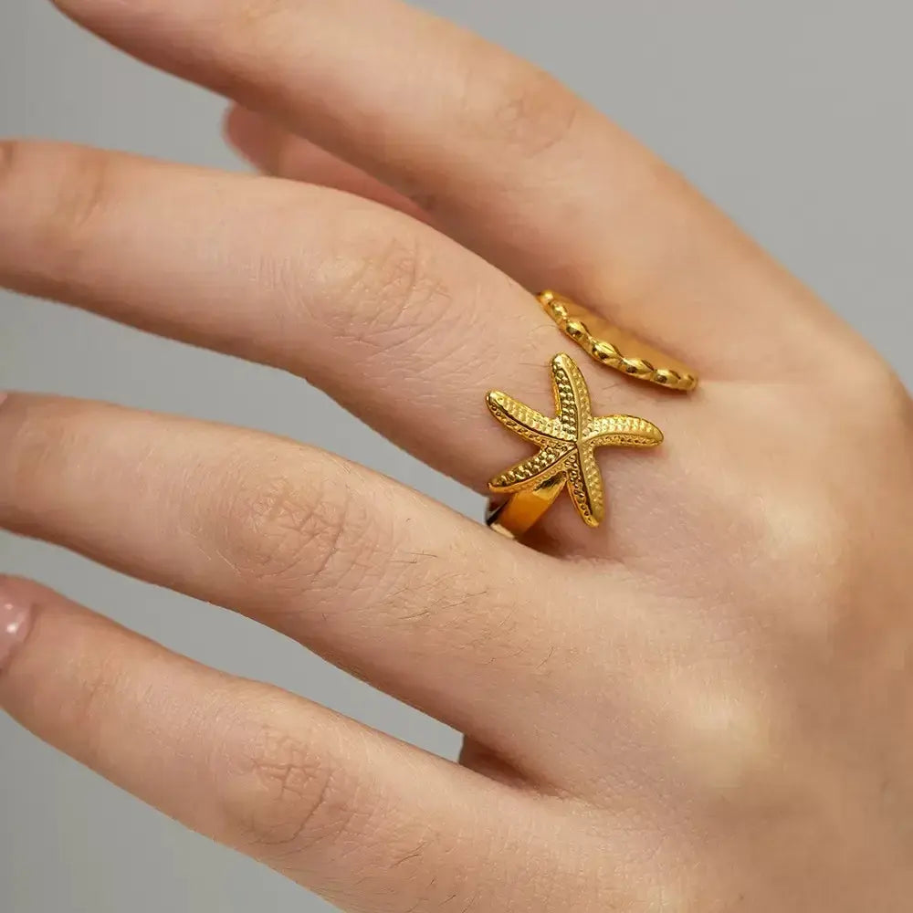 Starfish Gold Ring worn on a hand, featuring an open adjustable design with starfish and seashell ends in a clean neutral close-up | OriaJewel
