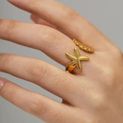 Starfish Gold Ring worn on a hand, featuring an open adjustable design with starfish and seashell ends in a clean neutral close-up | OriaJewel