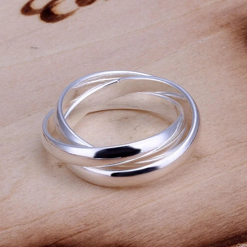 Shiny sterling silver crossover ring with intertwined bands on a light wooden surface | Oria Jewel