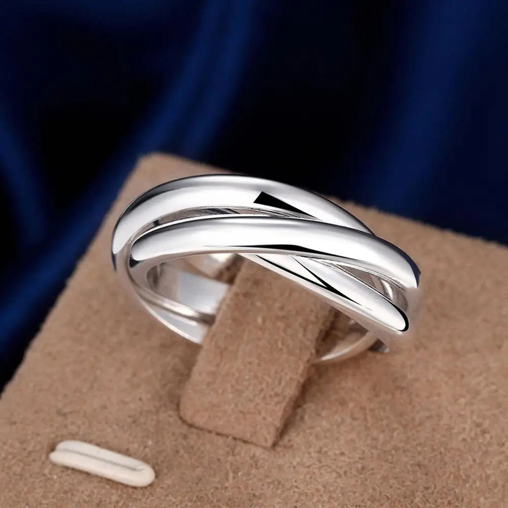 Shiny sterling silver crossover ring on tan display, dark blue background | Oria Jewel 
