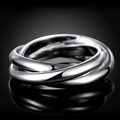 Shiny sterling silver crossover ring displayed on a light wooden surface | Oria Jewel