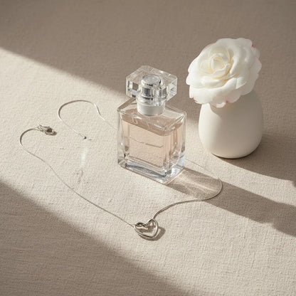 Elegant Sterling Silver Heart Chain Necklace beside perfume bottle and white flower on beige fabric — chic lifestyle setup | Oria Jewel