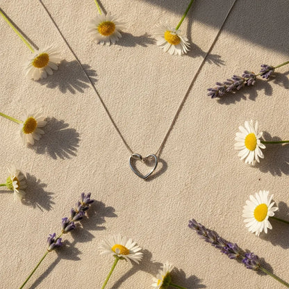 Flat-lay of Sterling Silver Heart Chain Necklace surrounded by daisies and lavender flowers under sunlight | Oria Jewel