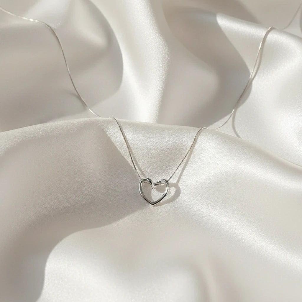Minimalist Sterling Silver Heart Chain Necklace displayed on soft satin fabric — delicate shine and romantic design | Oria Jewel