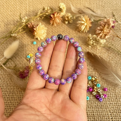 Hand holding the colorful Stress Relief Gemstone Bracelet over a rustic fabric background with dried flowers and beads | Oria Jewel