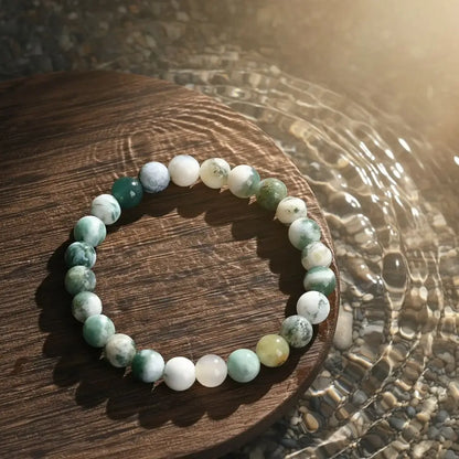 Success Energy Stone Bracelet resting on a round wooden platform surrounded by rippling water, with sunlight reflecting off the polished green and white beads to suggest calm and flow | Oria Jewel