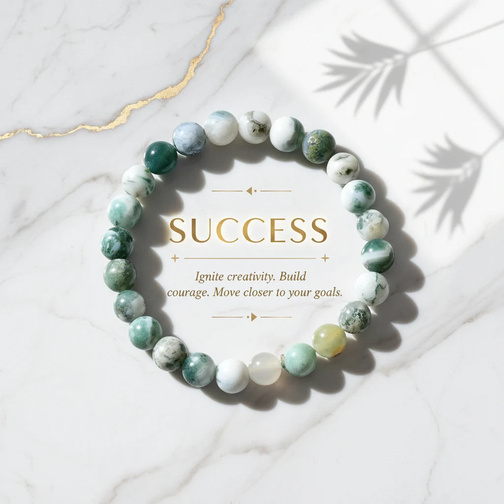 Flat-lay of a Success Energy Stone Bracelet arranged in a circle on white marble with gold lettering reading “SUCCESS” and an inspirational message, emphasizing motivation, creativity, and goal-focused energy | Oria Jewel