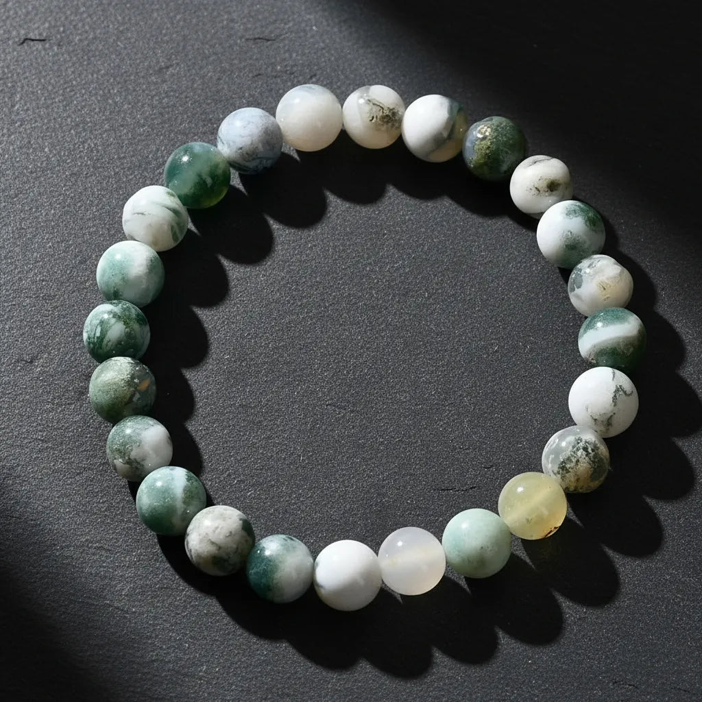 Dramatic close-up of the Success Energy Stone Bracelet on a dark textured surface with angled lighting that creates deep shadows and highlights the marbled green and white gemstone beads | Oria Jewel