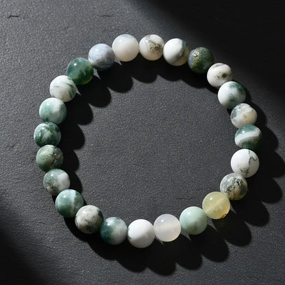 Dramatic close-up of the Success Energy Stone Bracelet on a dark textured surface with angled lighting that creates deep shadows and highlights the marbled green and white gemstone beads | Oria Jewel