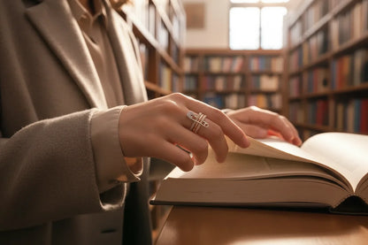 Close-up lifestyle shot of a hand flipping pages in a cozy library, highlighting the safety pin motif and tri-color bands with pavé sparkle — Tri-Color Safety Pin Ring | OriaJewel