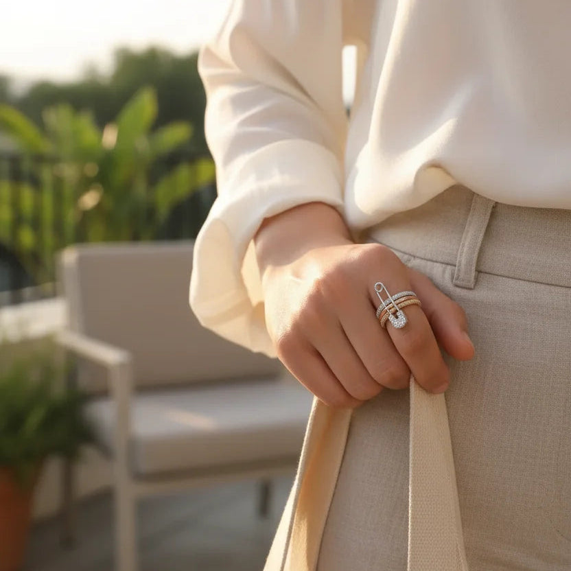 Outdoor golden-hour lifestyle photo with a woman holding a tote bag, showing the safety pin front detail, pavé heart charm, and tri-color ring stack — Tri-Color Safety Pin Ring | OriaJewel
