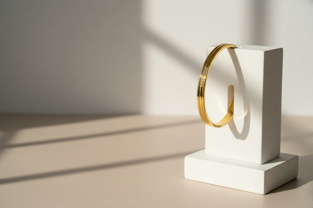 Triple Line Gold Hinged Bangle displayed vertically on a minimalist white stand, with soft natural sunlight and shadows highlighting its sleek triple-line design | Oria Jewel