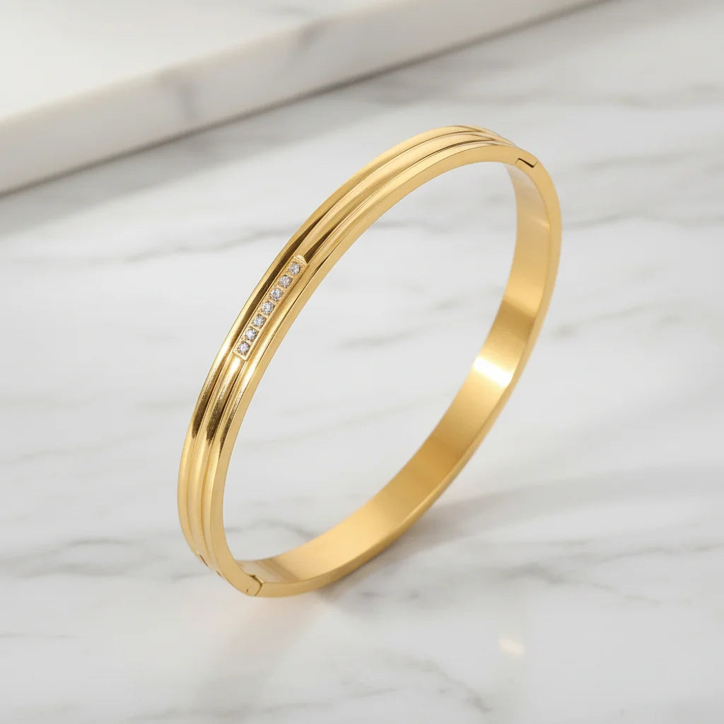 Close-up of the Triple Line Gold Hinged Bangle on a white marble surface, showcasing its smooth gold finish and delicate row of small clear stones | Oria Jewel