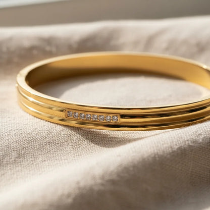 Macro shot of the Triple Line Gold Hinged Bangle resting on soft beige fabric, emphasizing the triple-line band detail and sparkling stone accents | Oria Jewel