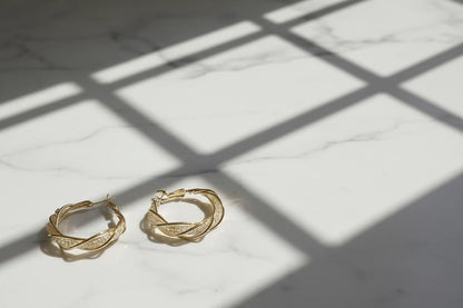 Twisted Crossover Hoop Earrings on marble with window shadows | OriaJewel
