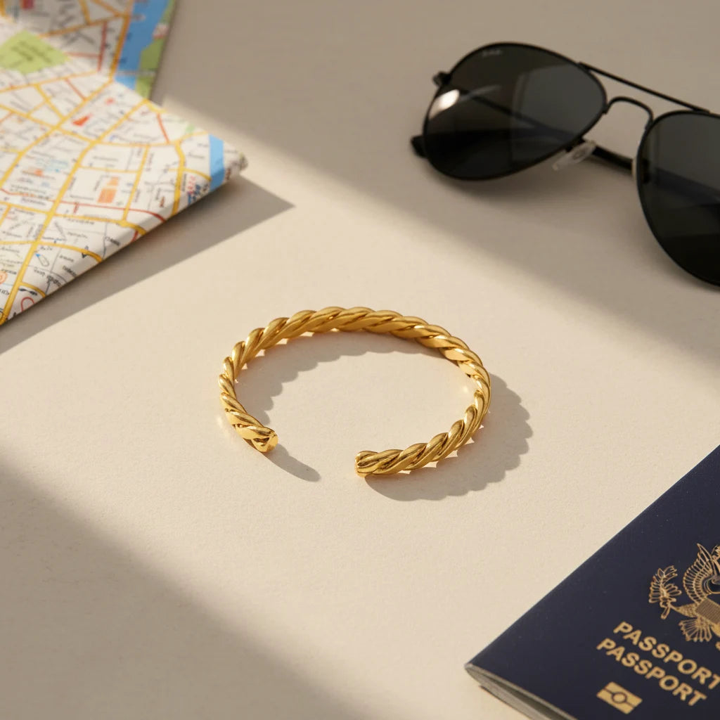 Flatlay of travel essentials on a light surface, featuring a Twisted Gold Cuff Bracelet beside a city map, sunglasses, and a passport, styled to suggest a chic jetsetter ready for a weekend getaway | Oria Jewel