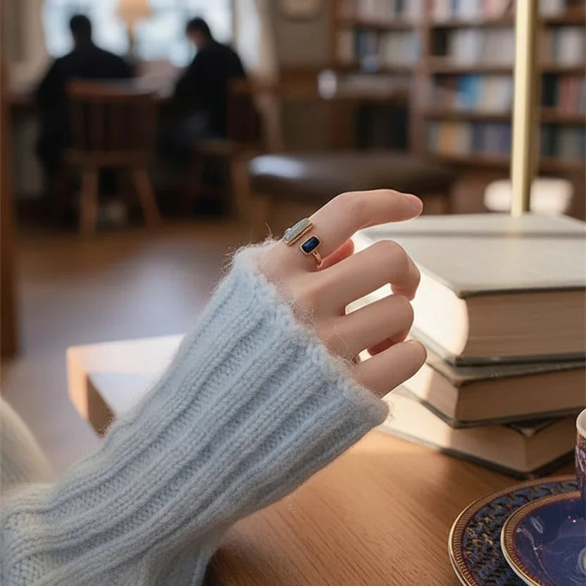 Two Stone Open Ring on a hand in a cozy library setting, soft focus books behind, highlighting the open band and the two rectangular stones | OriaJewel