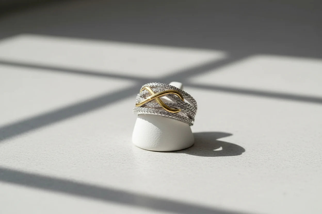 Two Tone Criss Cross Ring displayed on a small white ring stand under window-grid shadows, clean studio scene emphasizing the layered pavé rows and gold criss-cross centerpiece | OriaJewel