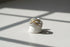 Two Tone Criss Cross Ring displayed on a small white ring stand under window-grid shadows, clean studio scene emphasizing the layered pavé rows and gold criss-cross centerpiece | OriaJewel