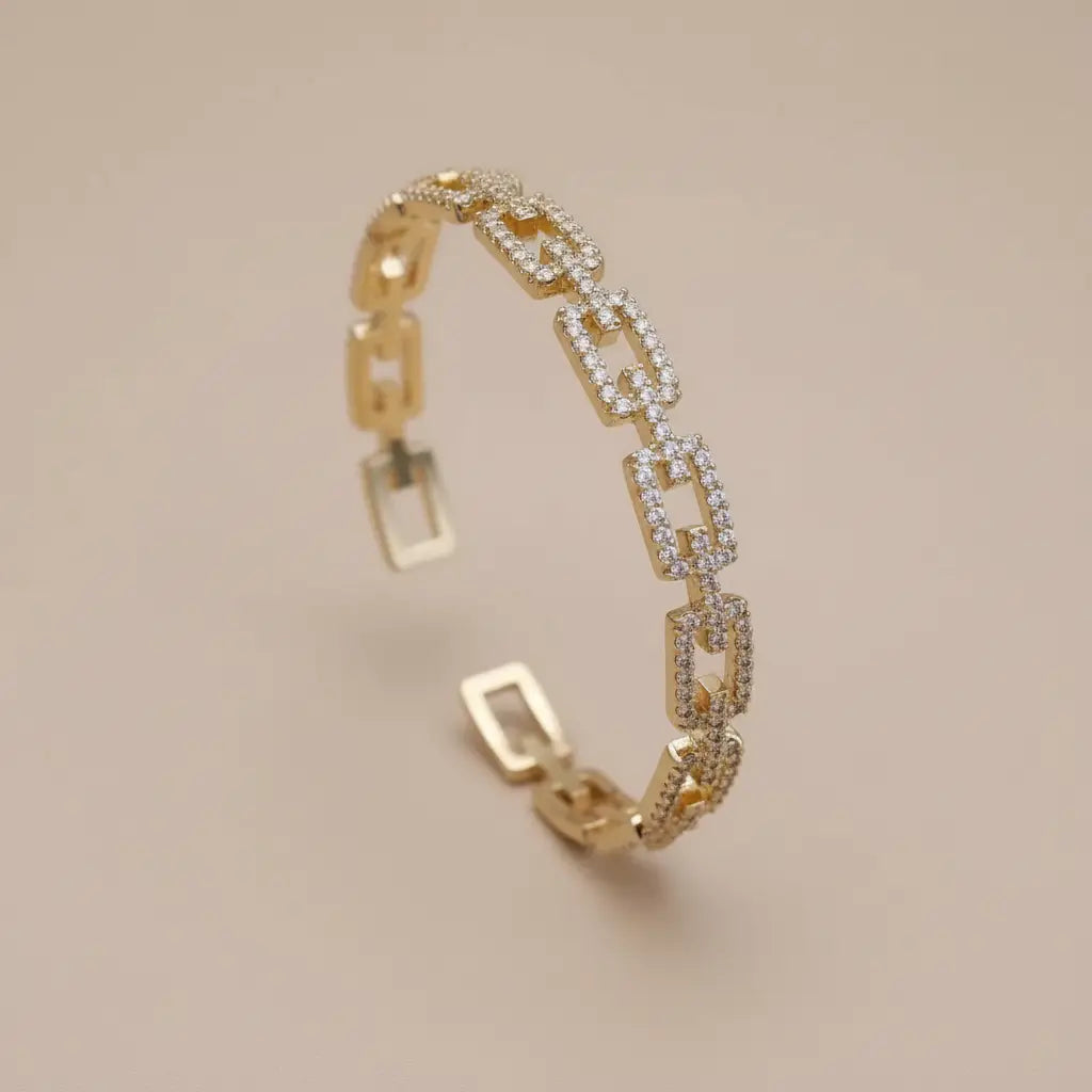 Veluxa Pavé Link Cuff in gold displayed upright on a soft beige background, showing open geometric links and sparkling pavé crystals | Oria Jewel