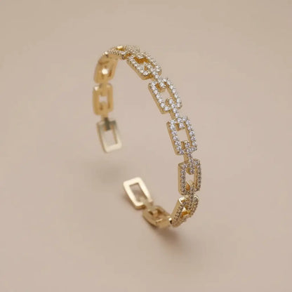 Veluxa Pavé Link Cuff in gold displayed upright on a soft beige background, showing open geometric links and sparkling pavé crystals | Oria Jewel