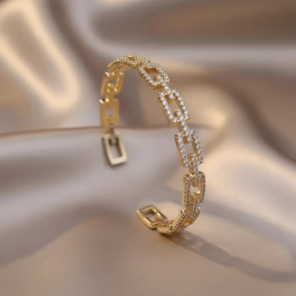 Veluxa Pavé Link Cuff in gold resting on champagne satin fabric, pavé crystal links catching the light for a luxurious glow | Oria Jewel