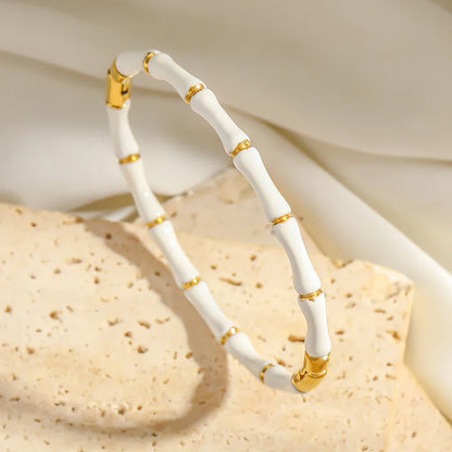 Close-up of a White Bamboo bangle Bracelet with gold accents draped over a textured stone, highlighting its smooth enamel and organic bamboo shape | Oria Jewel