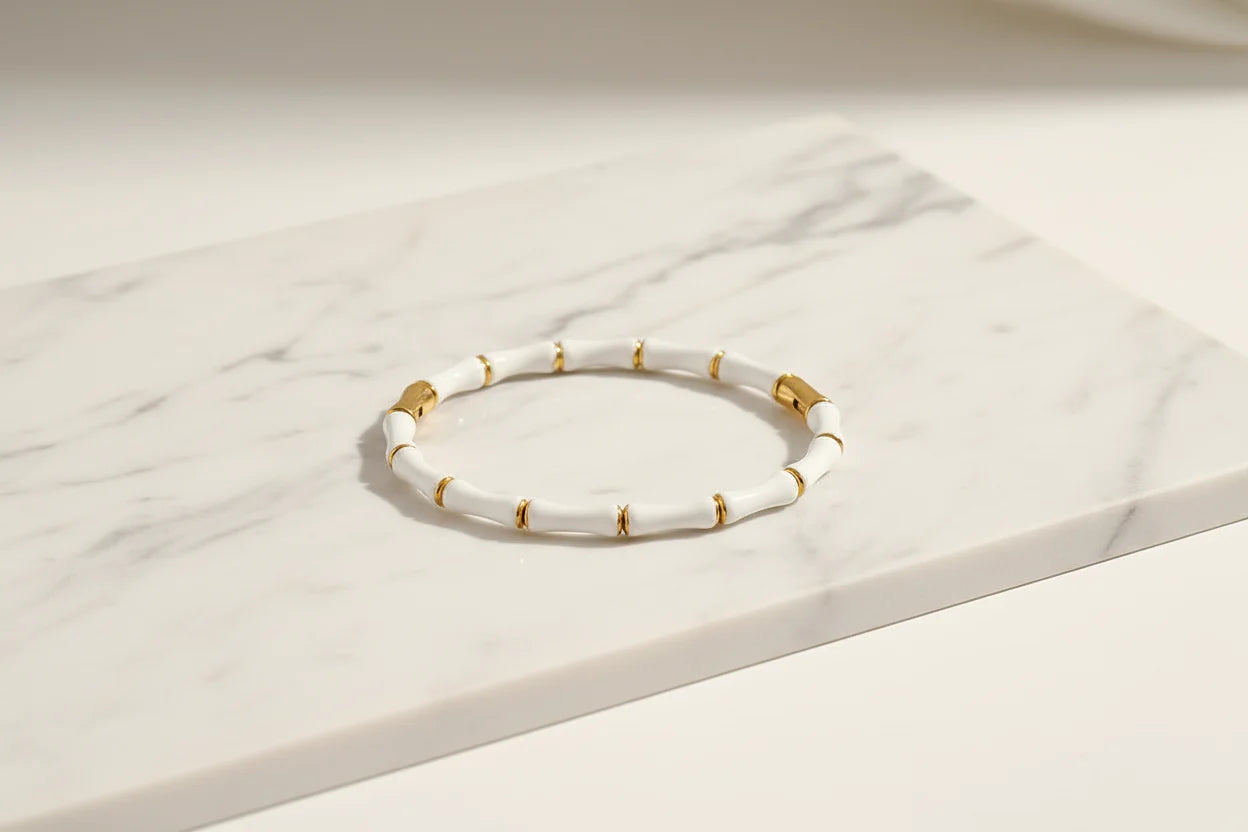 White Bamboo bangle Bracelet with gold detailing laid flat on a white marble slab, showing the sleek bamboo segments and polished finish | Oria Jewel