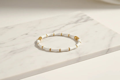 White Bamboo bangle Bracelet with gold detailing laid flat on a white marble slab, showing the sleek bamboo segments and polished finish | Oria Jewel